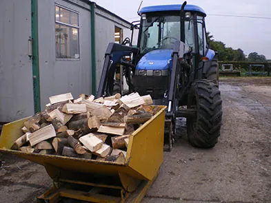 A tractor with a front loader full of split logs in the yard